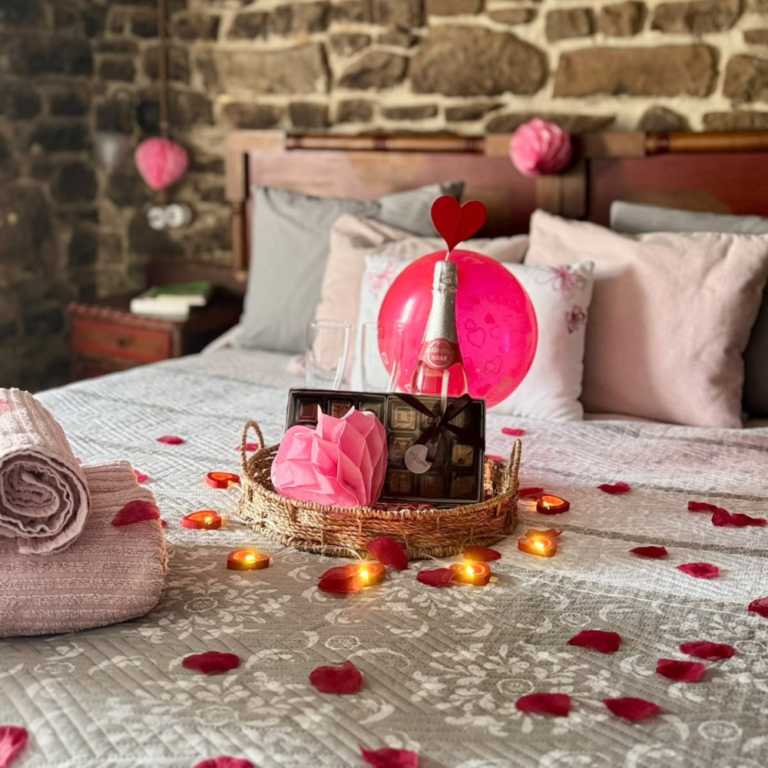 Detalle de bombones, sidra espumosa rosé y decoración romántica sobre una cama de La Vallicuerra.