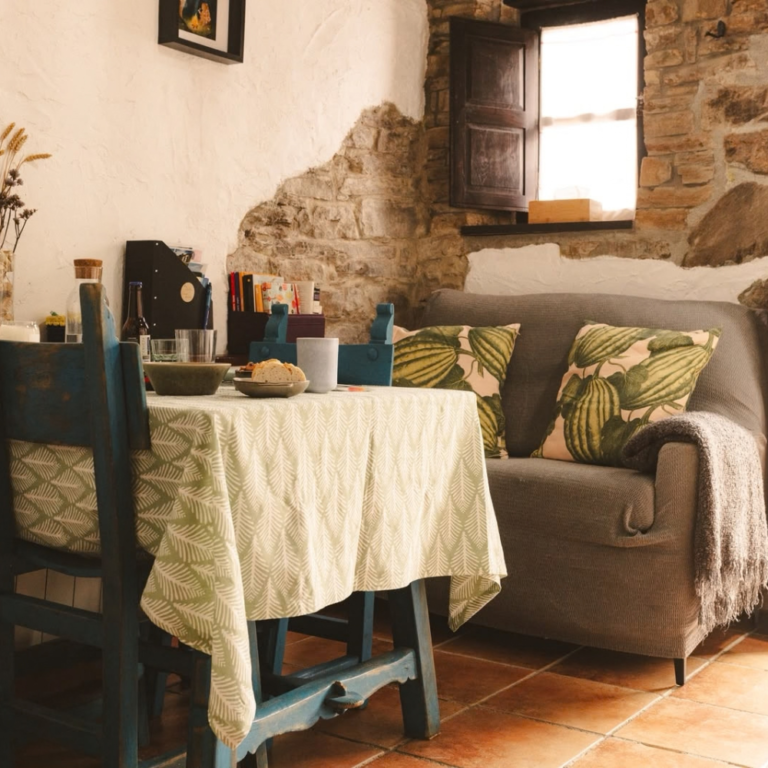 Zona de estar de un alojamiento rural de La Vallicuerra, con mesa, sofá y pared de piedra.